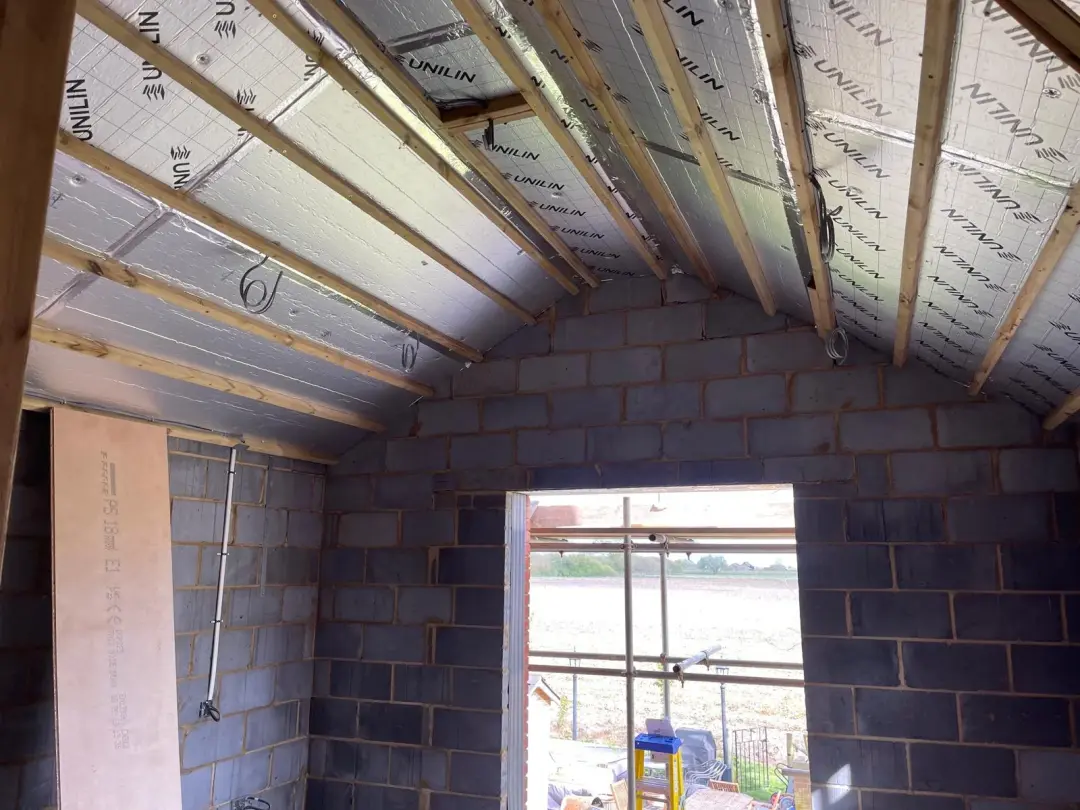 First-fix electrical cables looped between insulated roof rafters above blockwork walls