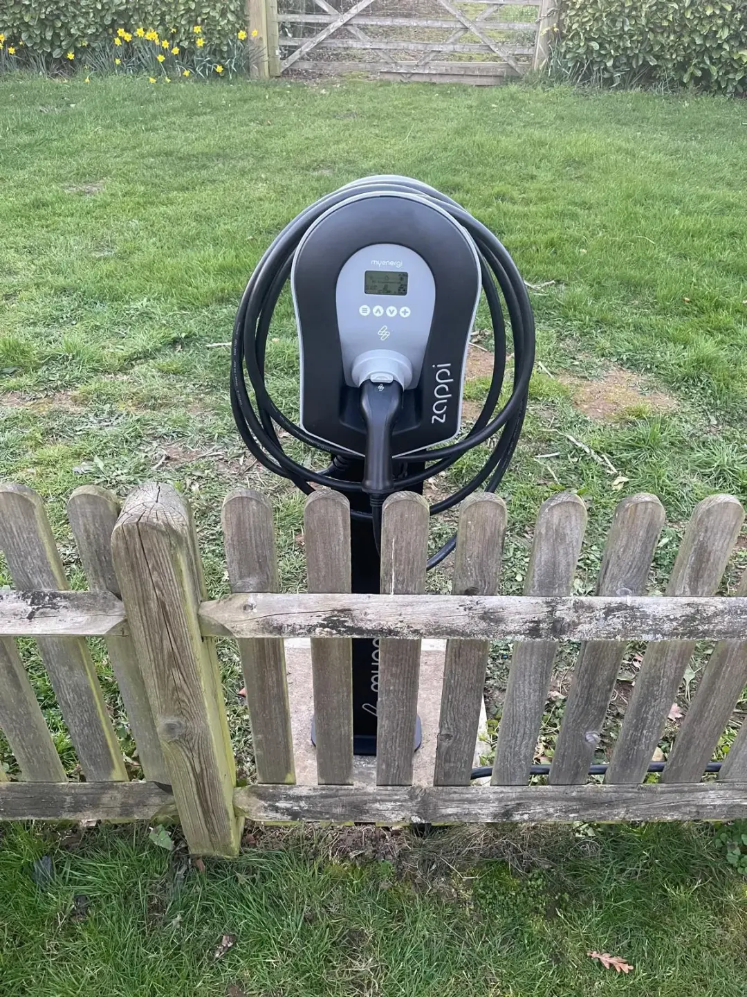 Zappi electric vehicle charger on a pedestal behind a wooden picket fence