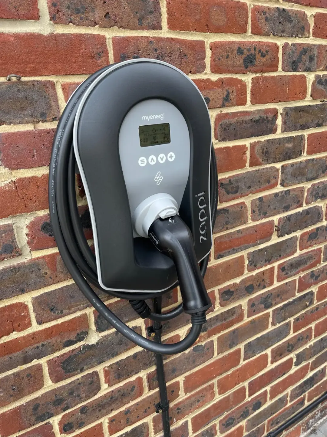 Wall-mounted Zappi EV charger with coiled charging cable on a red brick wall