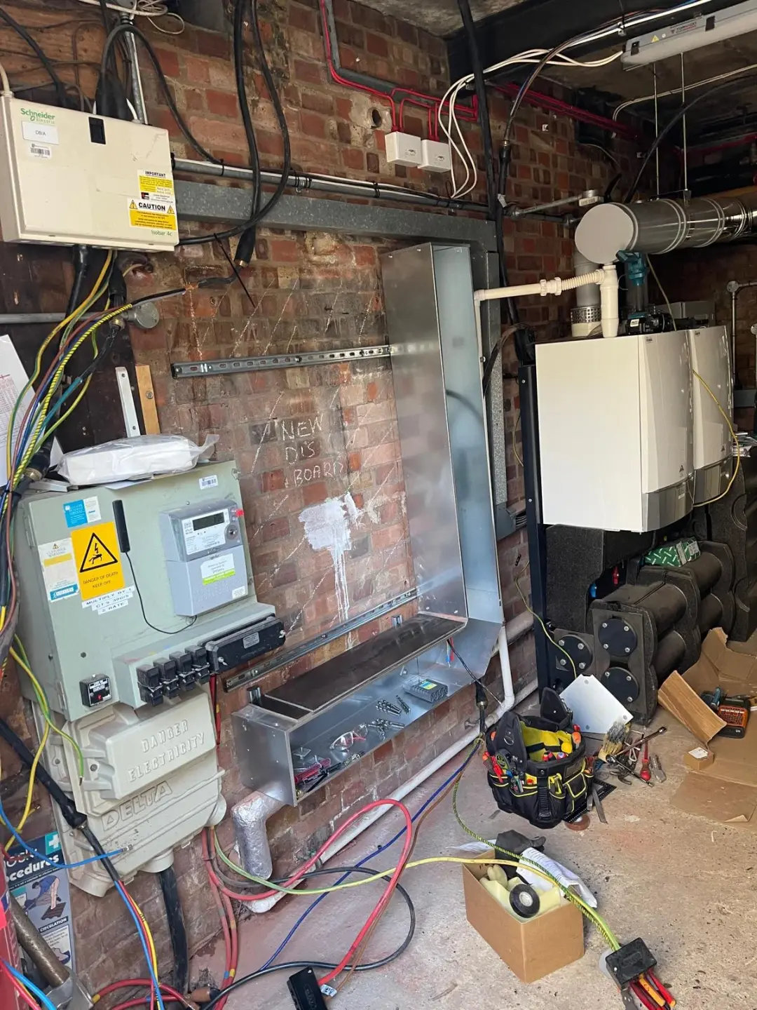 Electrical distribution board installation in progress beside boilers in a brick plant room
