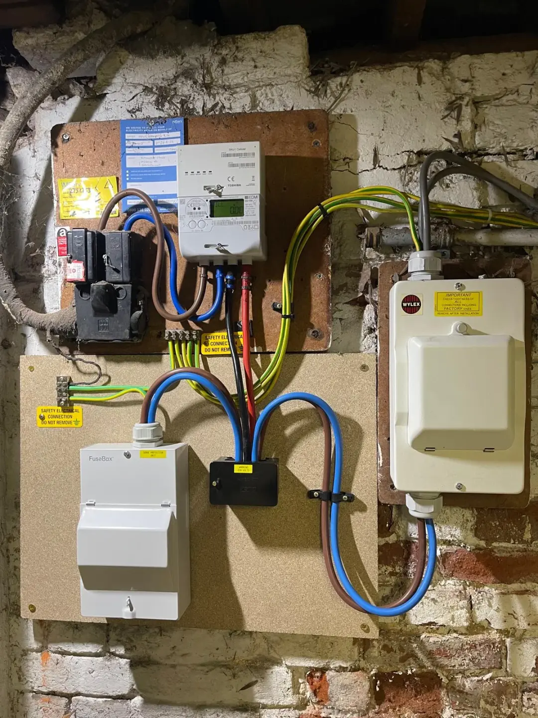Electricity meter with FuseBox and Wylex enclosures mounted on a brick wall